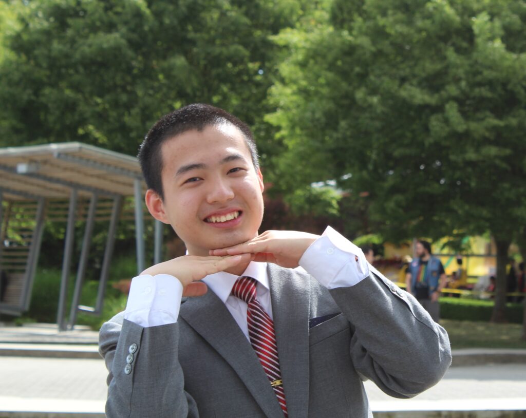 Jim, smiling, profile picture, hands under chin, green background with trees