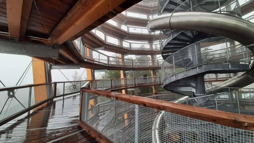 Photo taken while on the platform moving up in a spiral. Foggy background on the left with scenery obstructed, metal structure on the right that is a slide for people to slide down from the top.