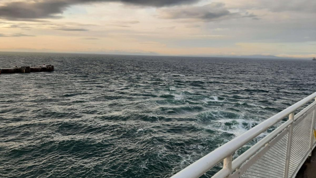 Photo taken by Jim, rail on the bottom right side with water and waves crashing filling up the page of the sea. The horizon edge line is slightly tilted in this photo.